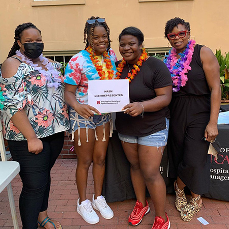 Members of HRSM REPRESENT hold up a sign with their organization's name at a fall semester welcome back lu'au .