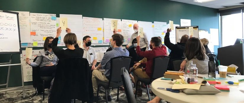 Group of UofSC leadership professionals wearing masks doing a group exercise in a classroom. An instructor is standing in front of the class. Participants are facing each other in chairs holding up pieces of paper with the numbers 1-5 on them.