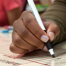 Close-up image of a hand holding a black marker pen and drawing a line graph on a whiteboard