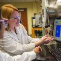 Student and professor wearing white lab coats and safety glasses conduct research in a lab