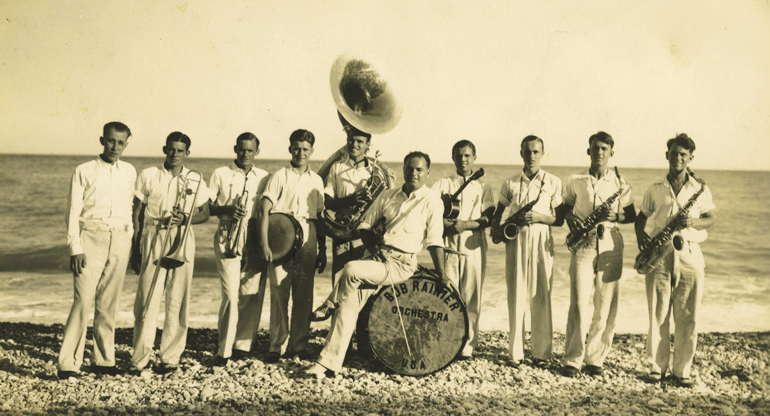 Musicians with various instruments pose for a photo on the beach