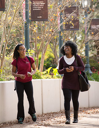 A faculty member and a student walking along outside laughing. 