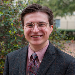 man with glasses, gray blazer with pink shirt and blue pink tie on