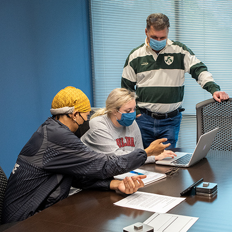 two students work on a laptop at a table with Tony Dillon