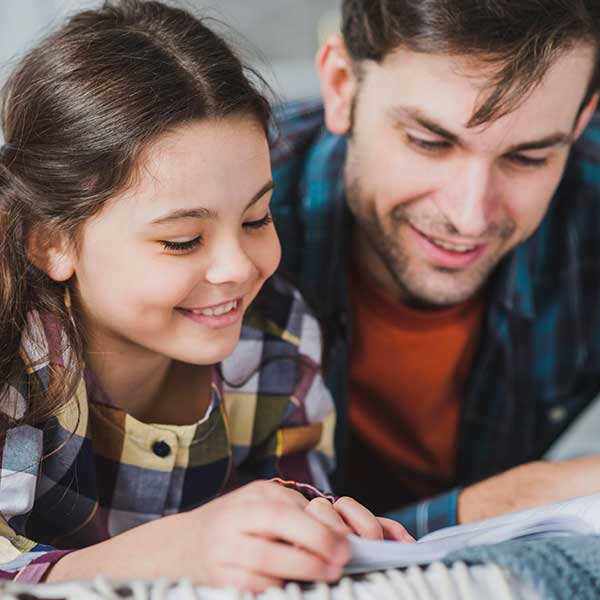 Adult male helps girl with book.