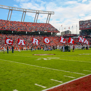 Cheerleaders run across a football field holding flags spelling out Carolina.