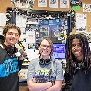 three students stand in a radio station booth